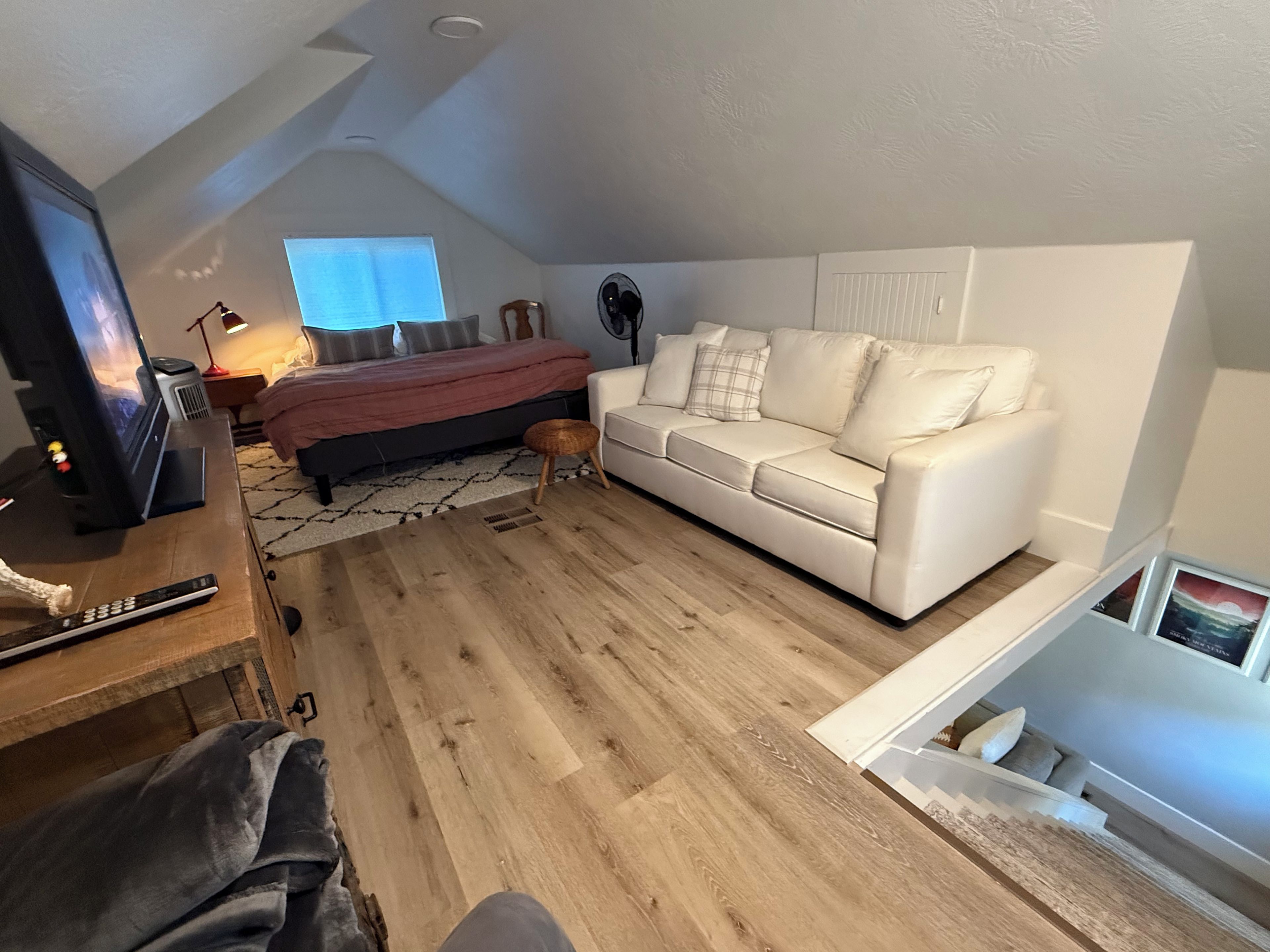 Ett sovrum med en säng, en vit soffa, ett trägolv, en tv och ett fönster.