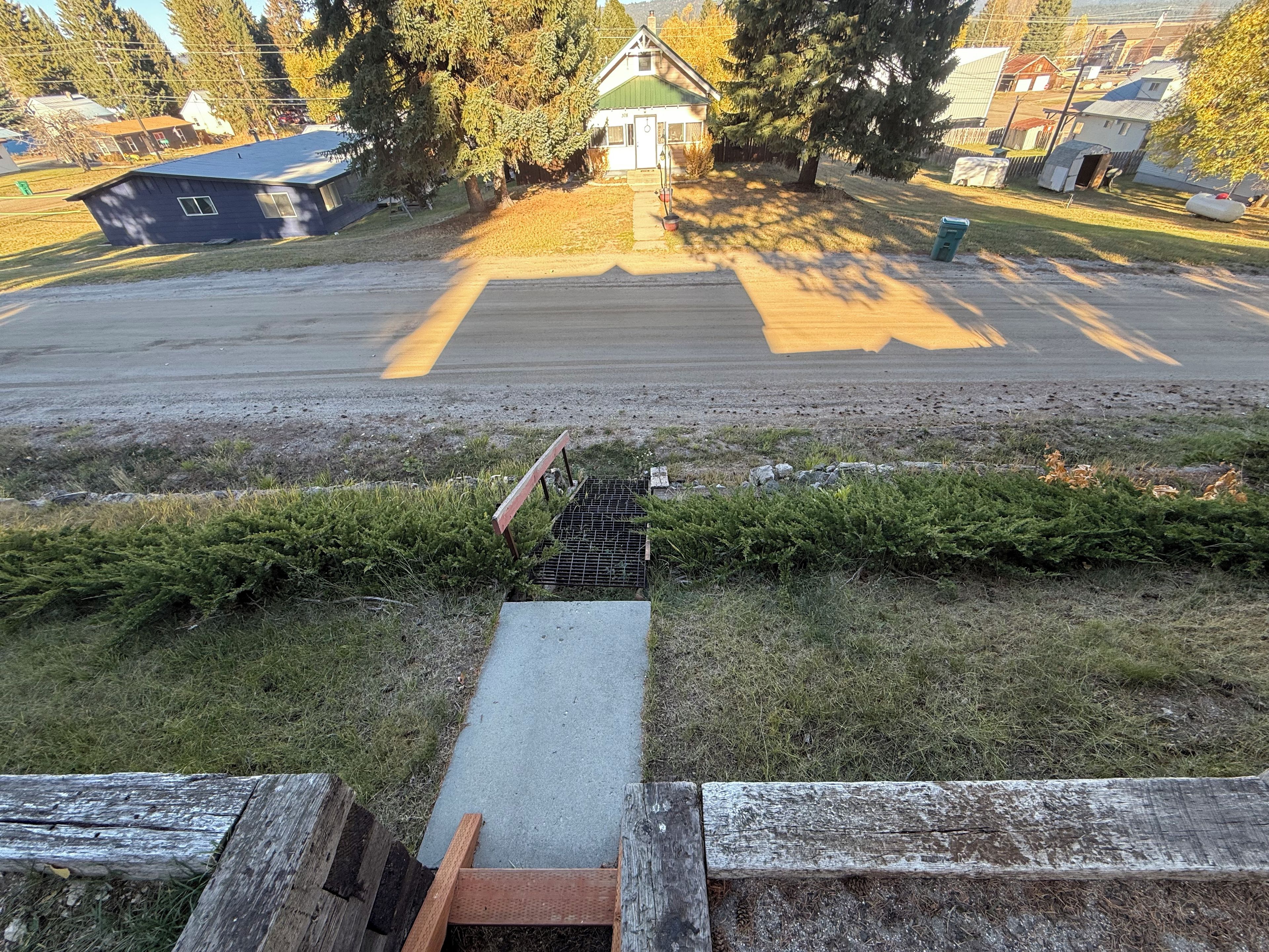 A residential area with a paved road, a small drainage grate, and a wooden fence.