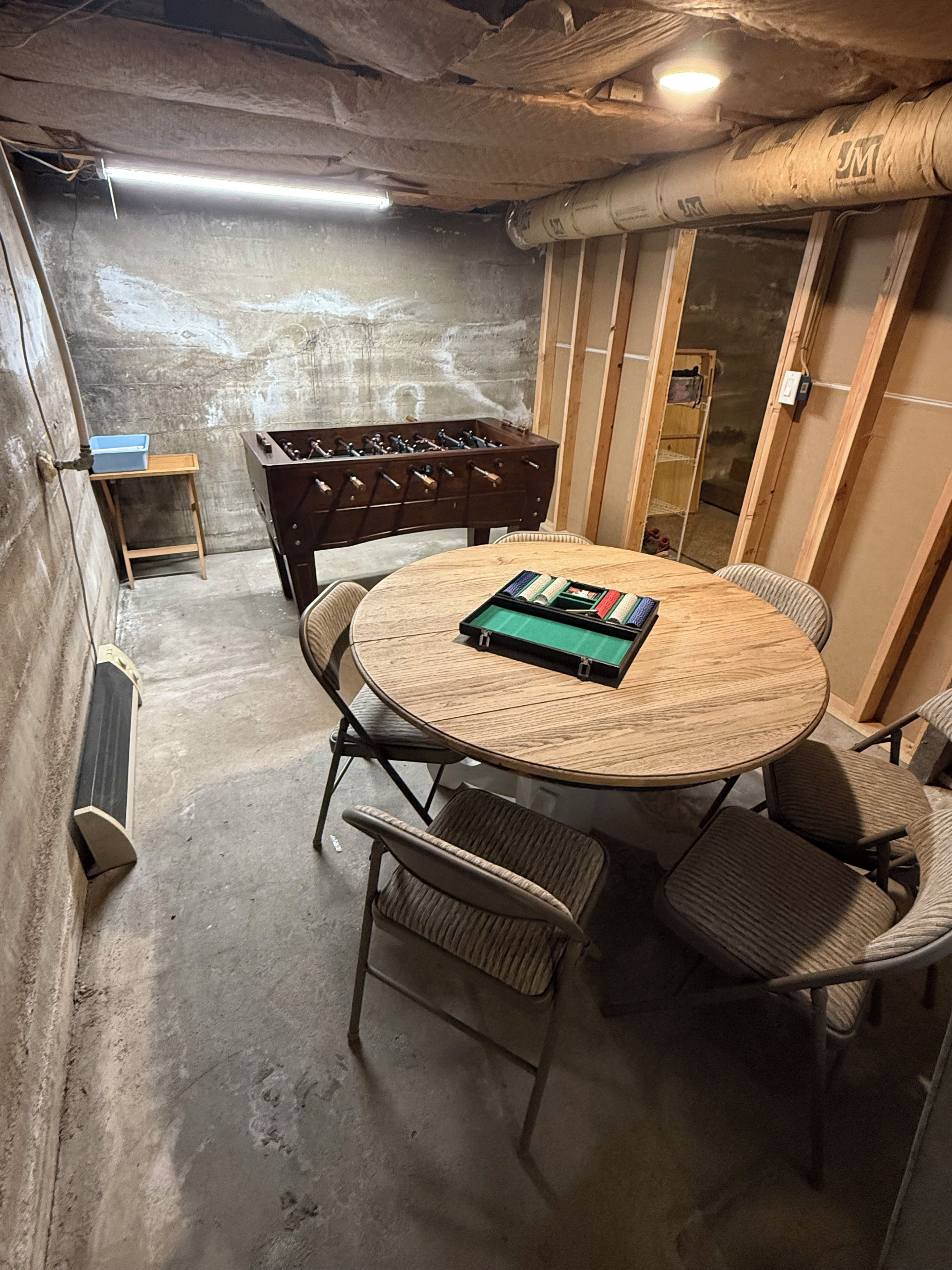A room with a round wooden table, four chairs, a foosball table, and a bookshelf.