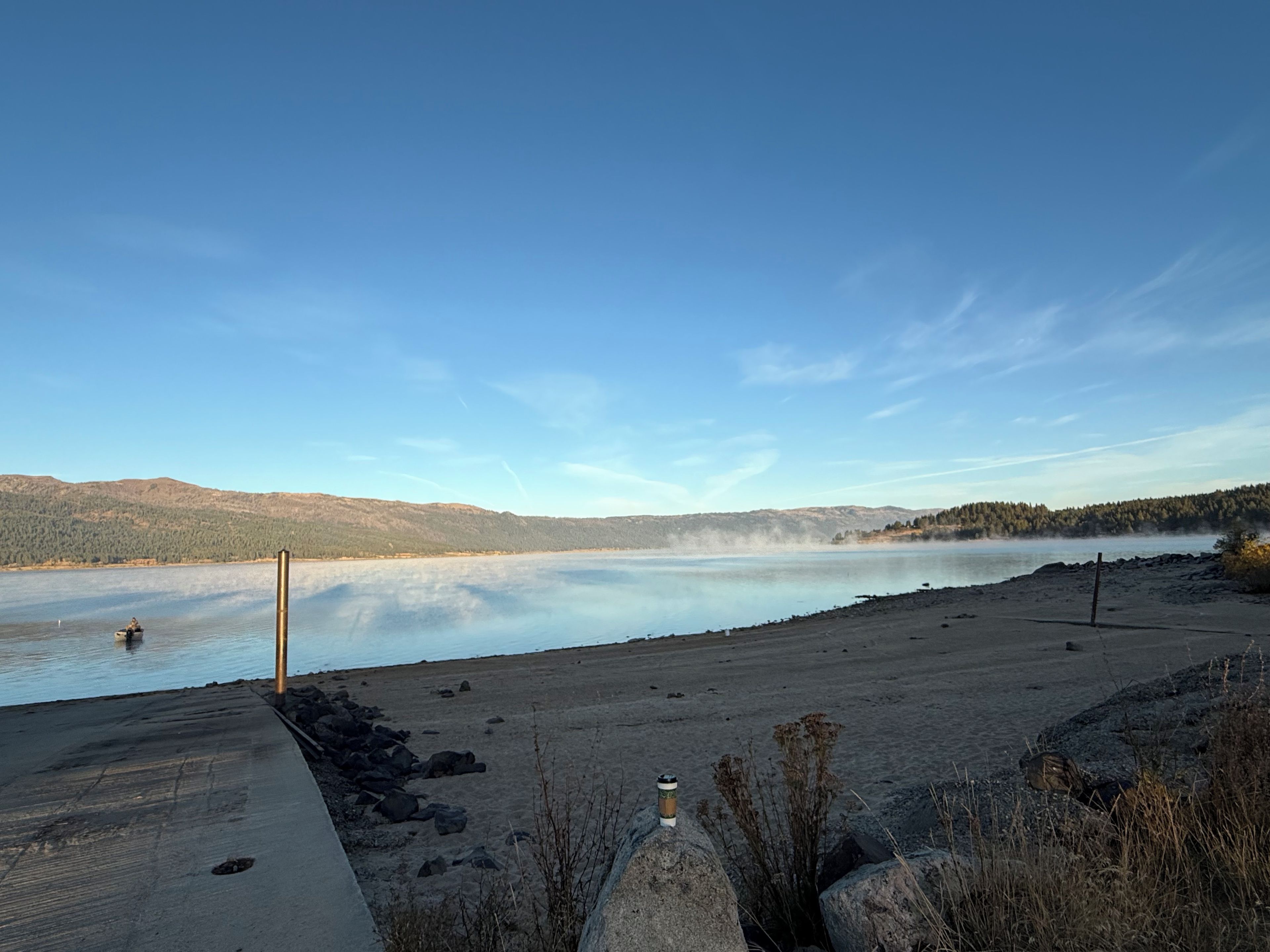 Une vue sur le lac, avec un quai en béton, une eau calme et des collines à l’horizon.