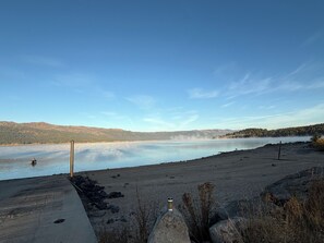 A lakeside view with a concrete dock, calm water, and distant hills.