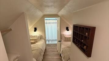 A narrow, sloped hallway with two beds on either side, a wooden floor, and a window at the end.