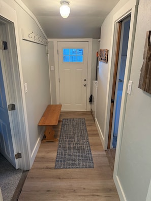 A hallway with a wooden bench, a rug, and a door with a window.