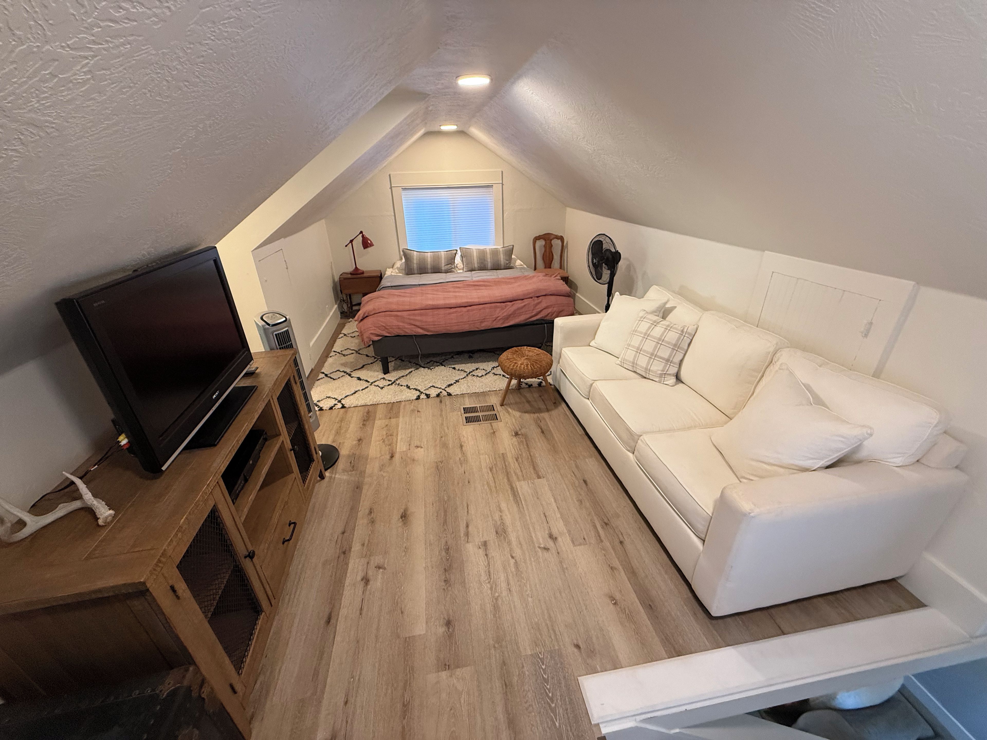A bedroom with a bed, a white sofa, a television, and a window.
