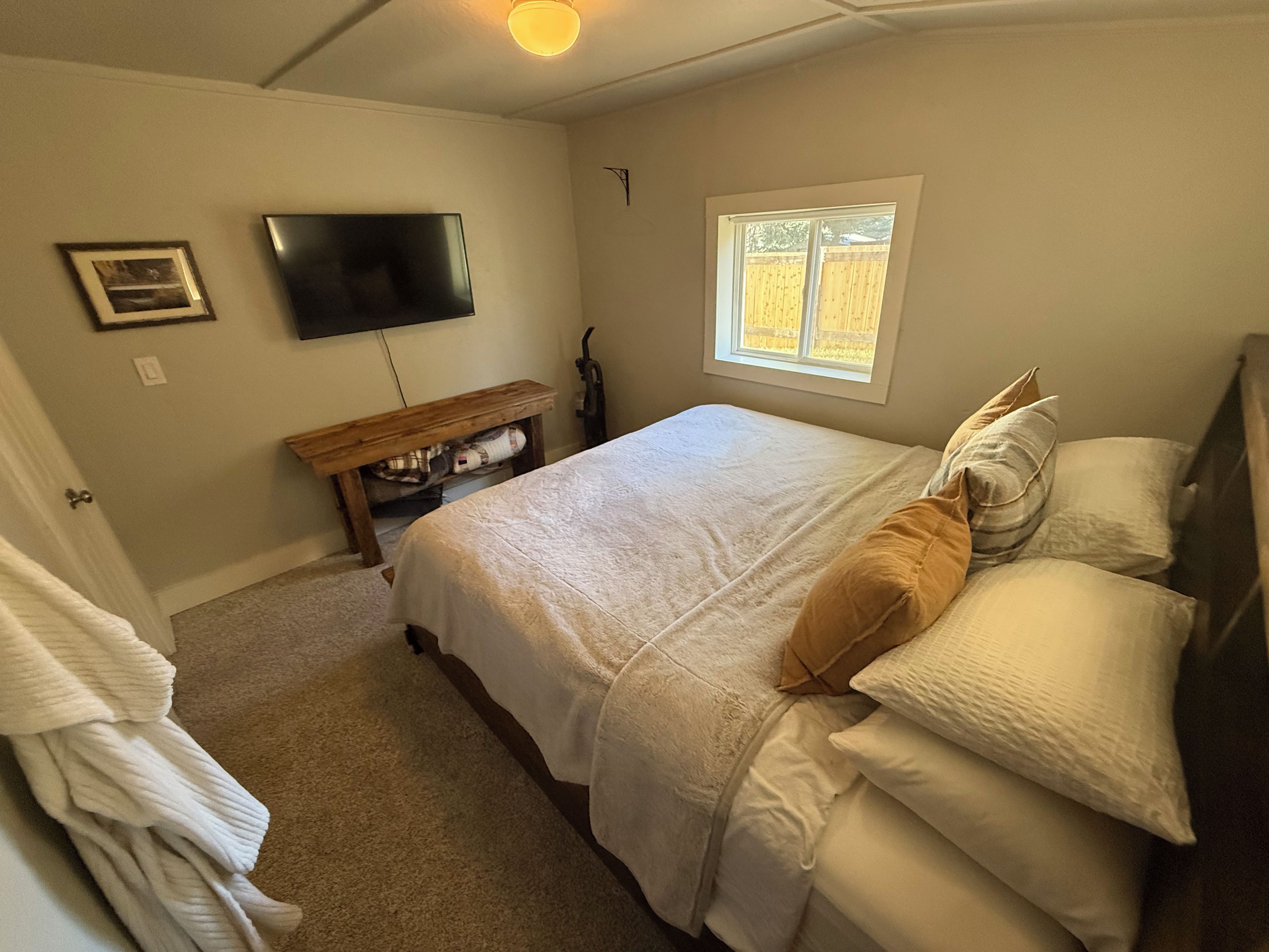Une chambre à coucher avec un lit, un téléviseur fixé au mur, une fenêtre et une porte.