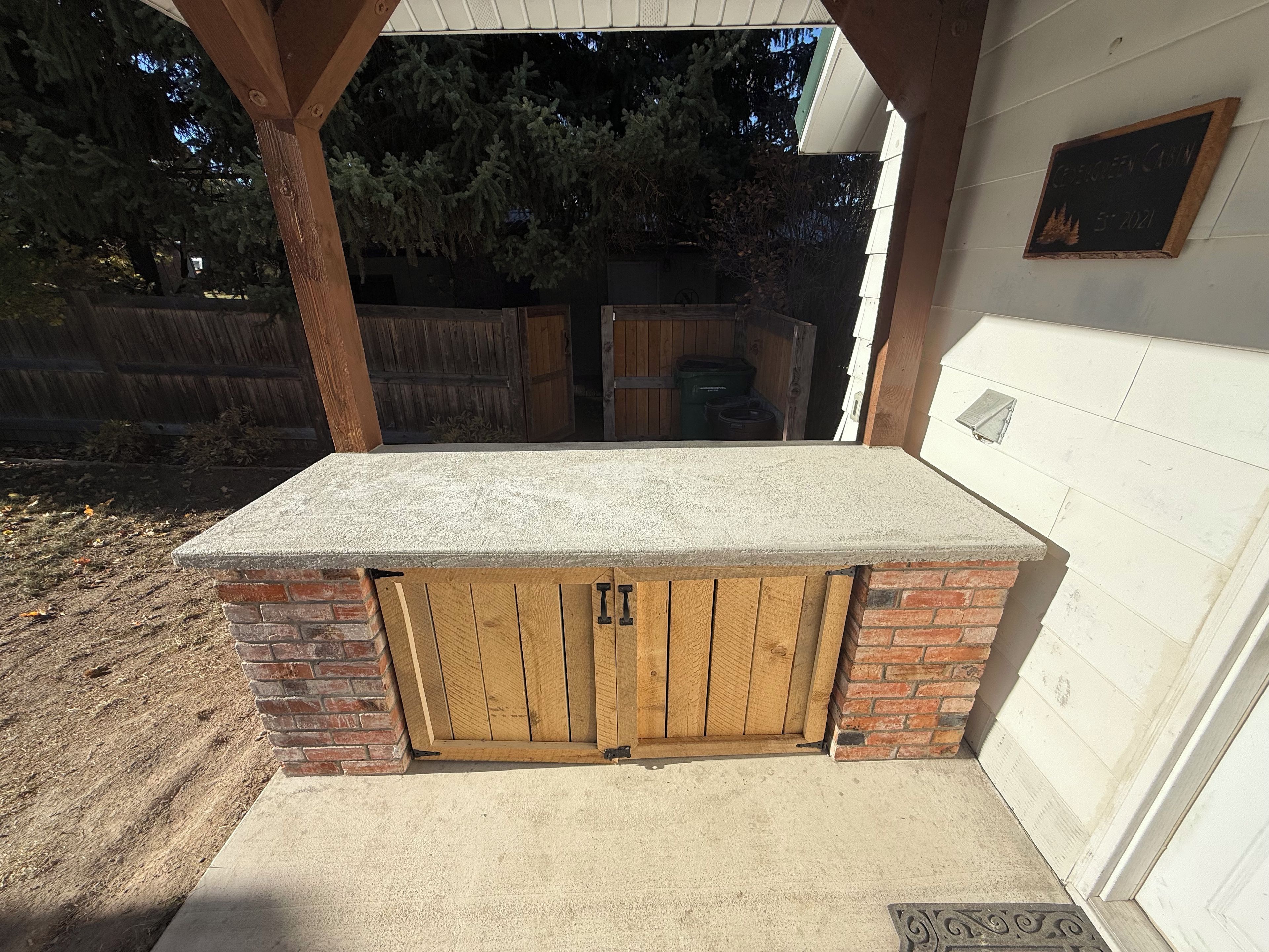Un espace extérieur abrité, doté d’un plan de travail en béton, de portes en bois et d’un mur en briques.