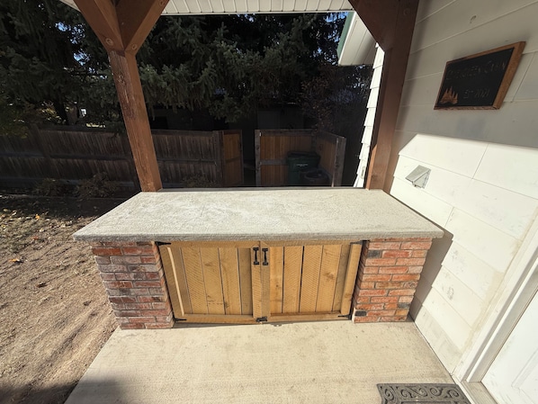 A covered outdoor area with a concrete countertop, wooden doors, and a brick wall.