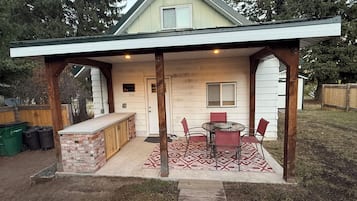 Une terrasse extérieure couverte, dotée d’un comptoir en briques et de chaises rouges.
