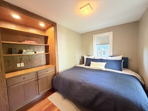 A bedroom with a bed, a wooden wardrobe, and a window.