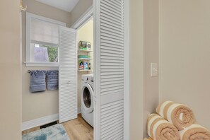 A laundry room with a washing machine, shelves with laundry supplies, and towels. - Serenity Retreat | Hot Tub + Fire Pit | Walk Downtown (West Hartford)