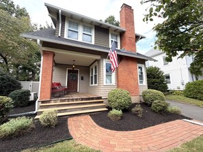 A two-story house with a front porch, a brick chimney, and a flag.