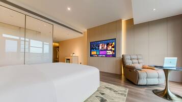 Un dormitorio moderno con una cama grande, un televisor montado en la pared, un sillón de cuero y una mesita con una computadora portátil.