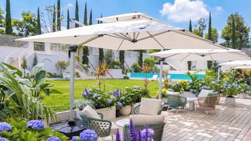 Terraza con mobiliario exterior y sombrillas, piscina al fondo y un jardín cuidado.