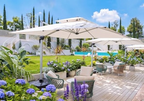 A deck with outdoor furniture and umbrellas, a swimming pool in the background, and a well-maintained garden.