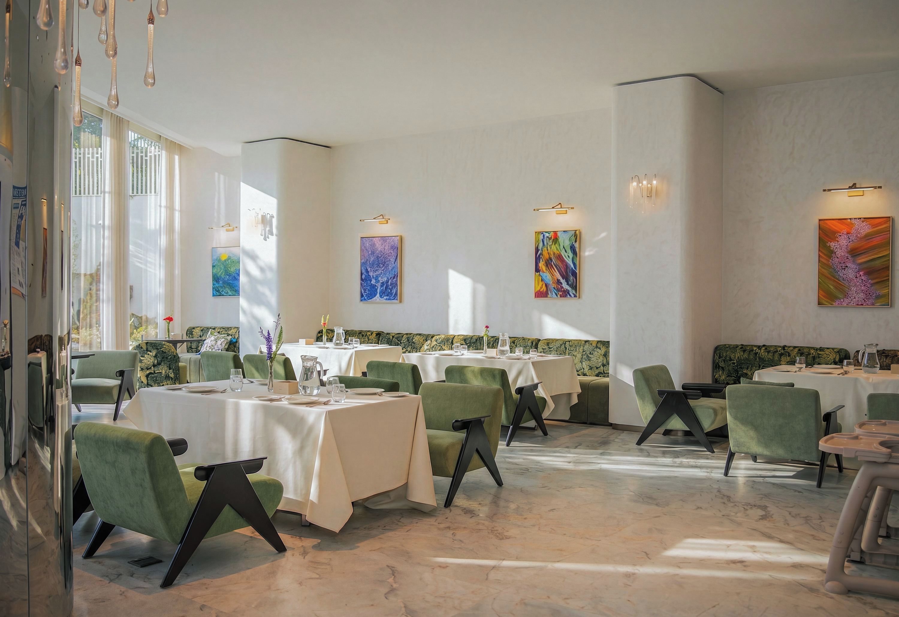 A restaurant with multiple tables, green chairs, and artwork on the walls.