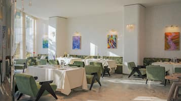 A restaurant with multiple tables, green chairs, and artwork on the walls.