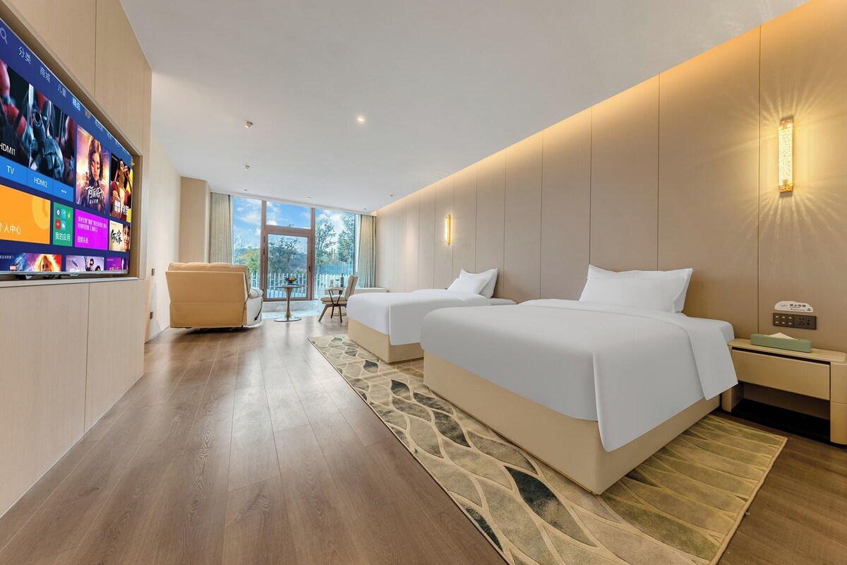 Ein Hotelzimmer mit großem Flachbildfernseher, zwei Betten, einer Sitzecke und Blick ins Freie.