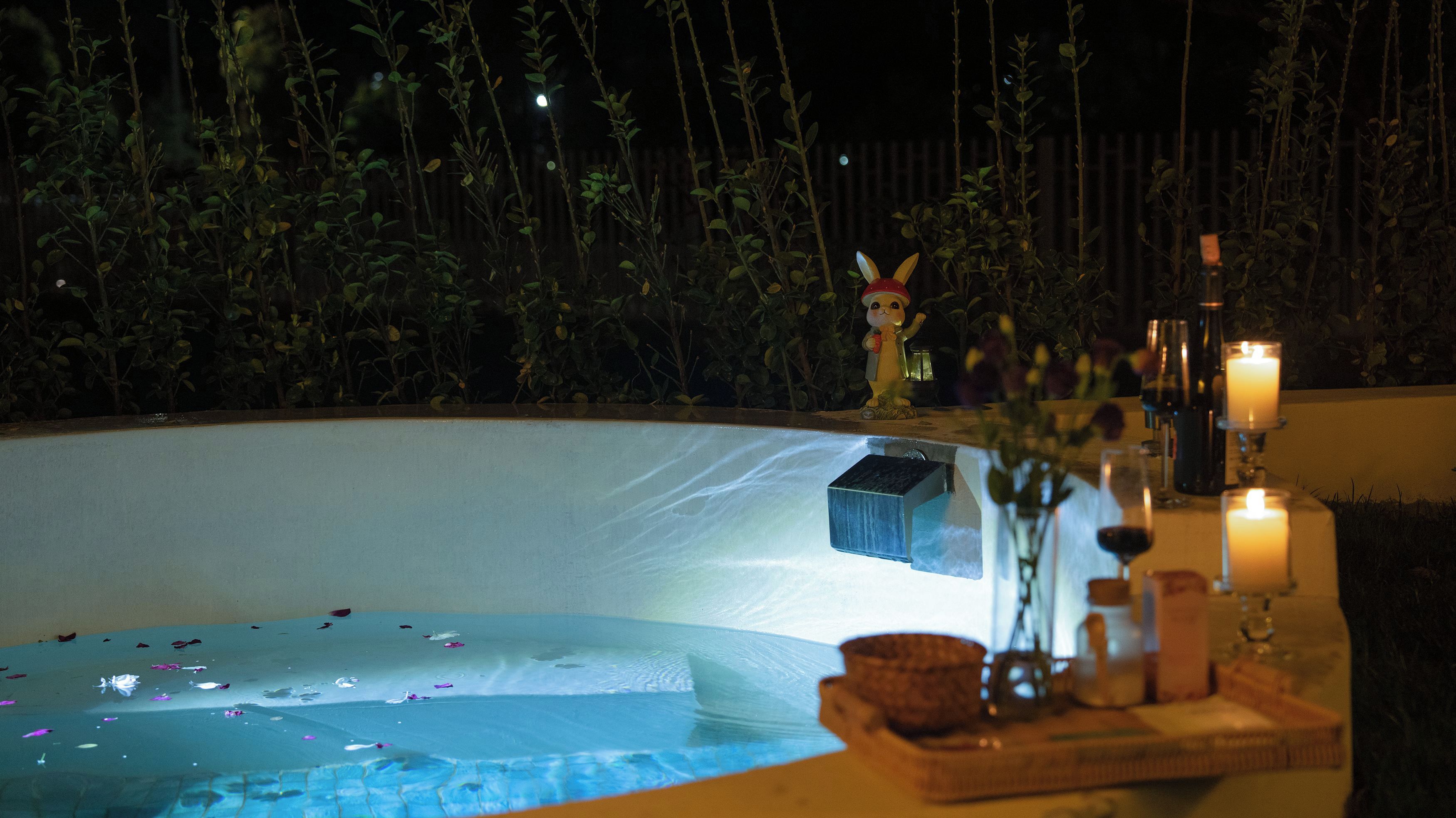 Un área de piscina con una estatua, velas y una mesa con un florero y cristalería.