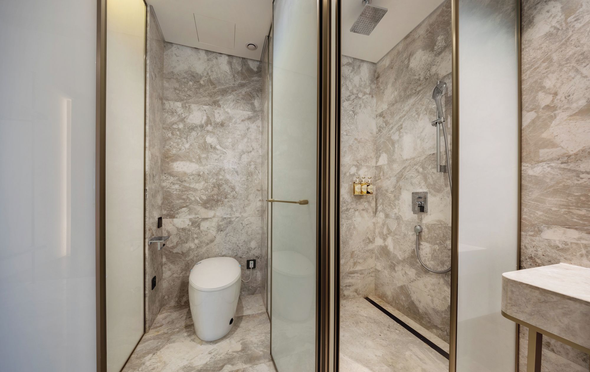 A modern bathroom with a glass-enclosed shower, marble walls, and a white toilet.