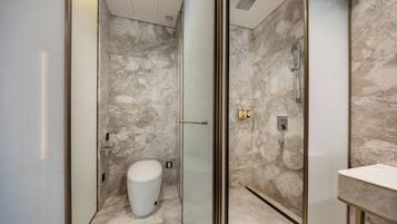 A modern bathroom with a glass-enclosed shower, marble walls, and a white toilet.