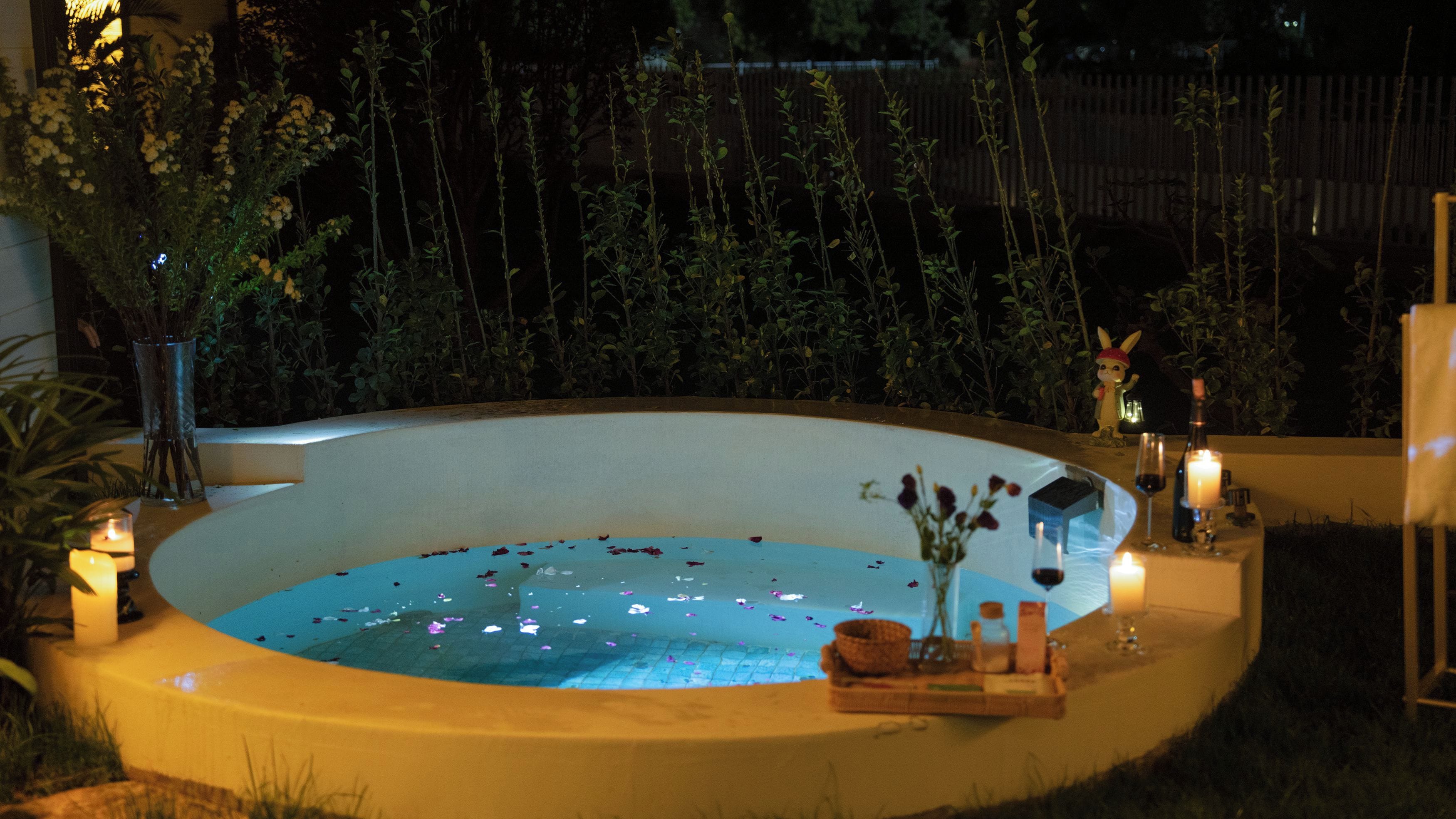 A circular outdoor pool with a fountain, surrounded by plants and candles.