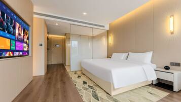 A modern hotel room with a large bed, bedside tables, a TV, and a digital clock.