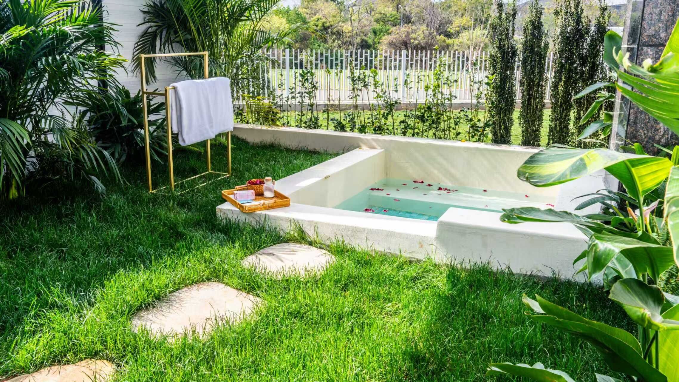 A garden with a small outdoor bathtub, surrounded by lush greenery and a white fence.