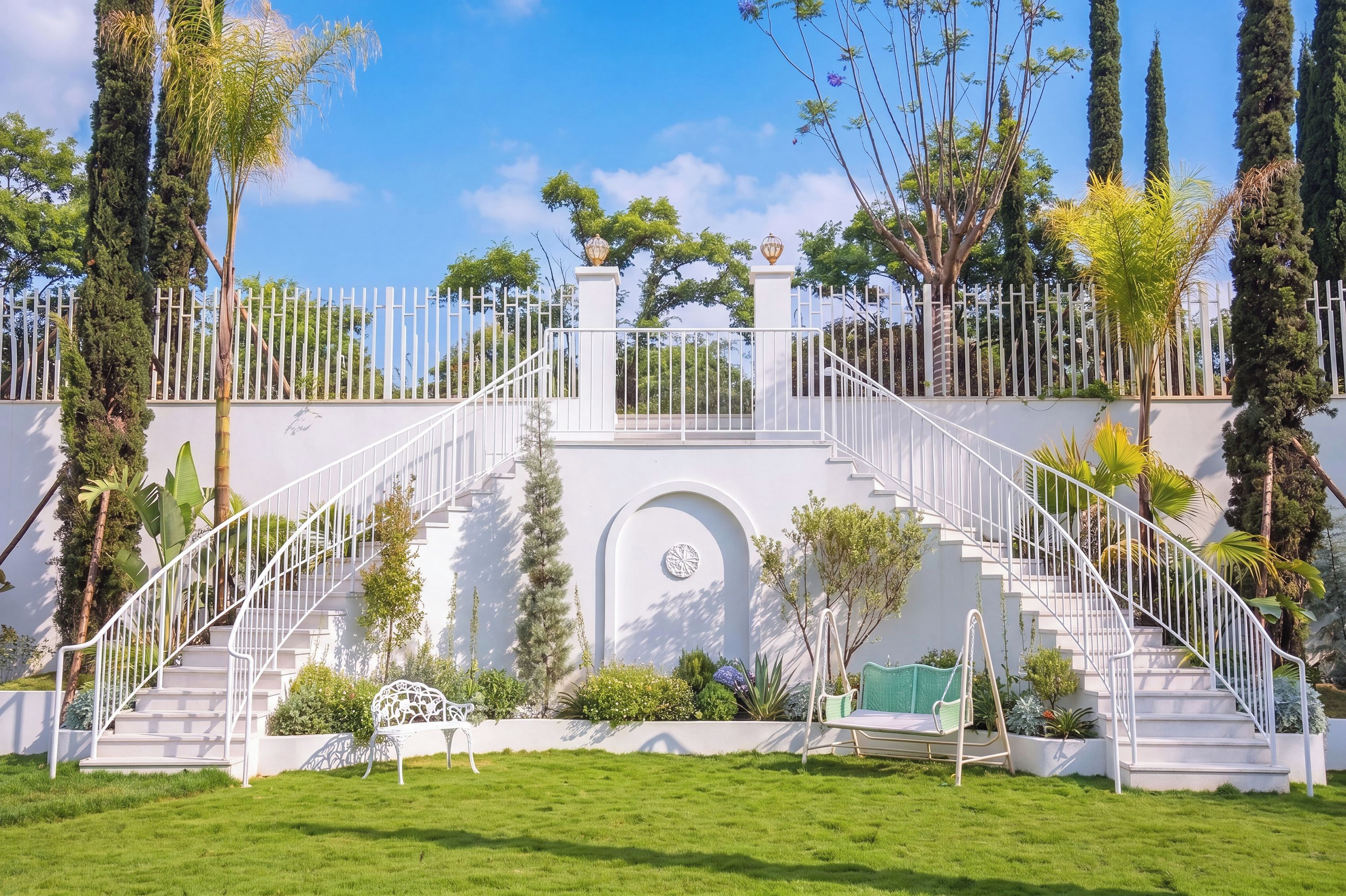 A white staircase leading to a gated entrance, surrounded by lush greenery and tall trees.