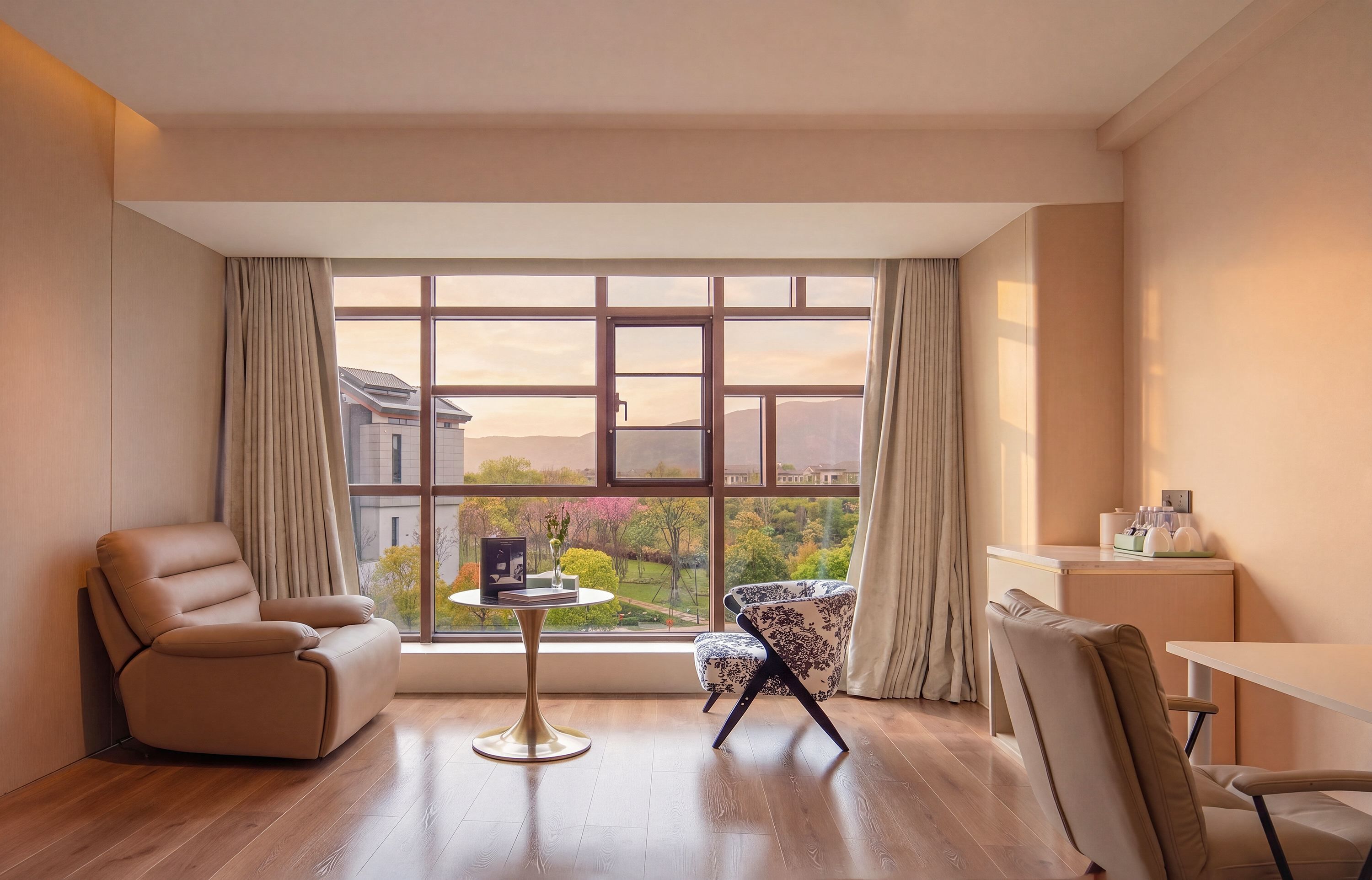 A modern room with a large window, a sofa, a chair, a small table, and a desk with a lamp.