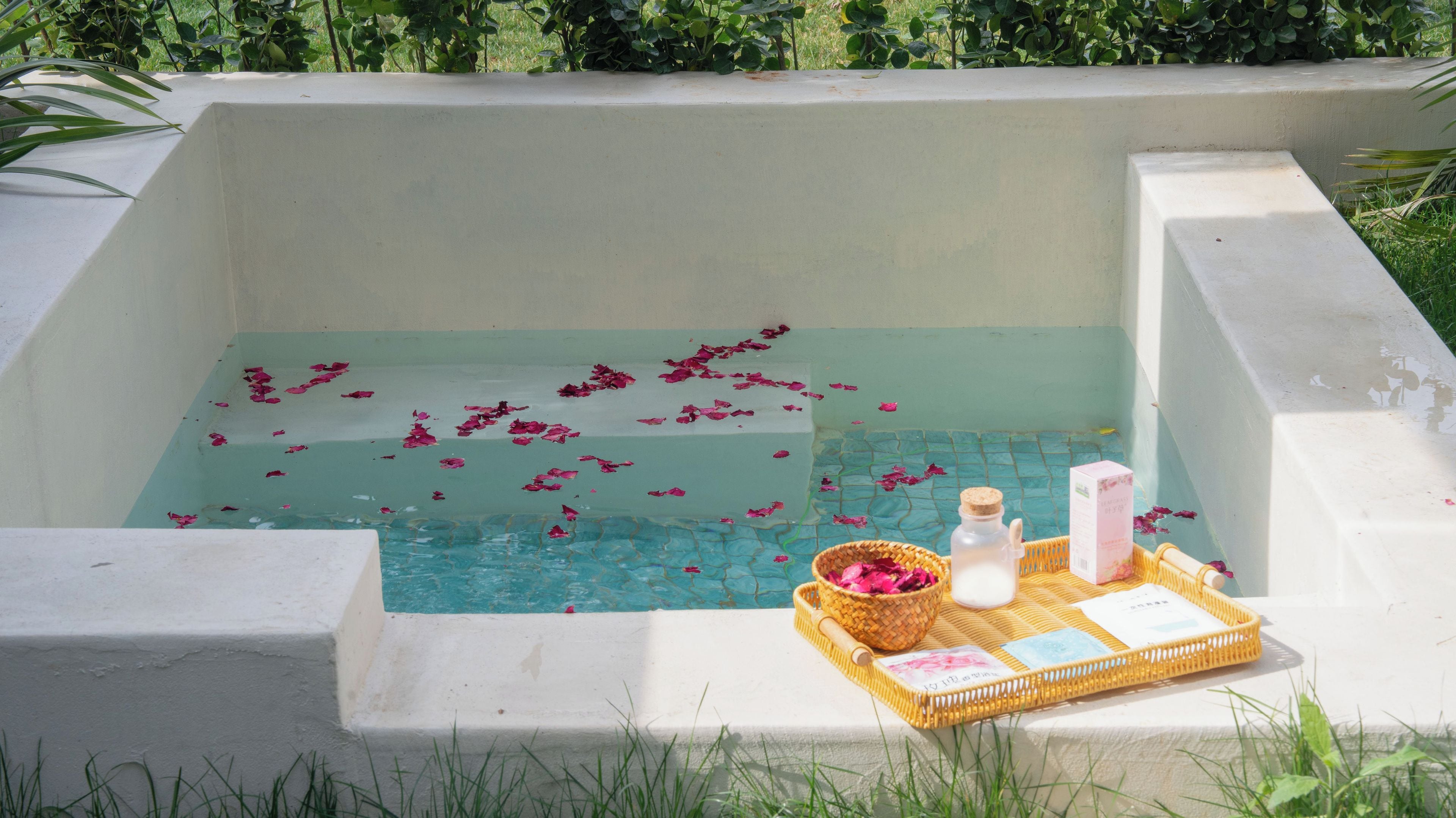 A rectangular pool with water and rose petals, surrounded by a white wall.