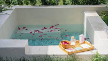 A rectangular pool with water and rose petals, surrounded by a white wall.