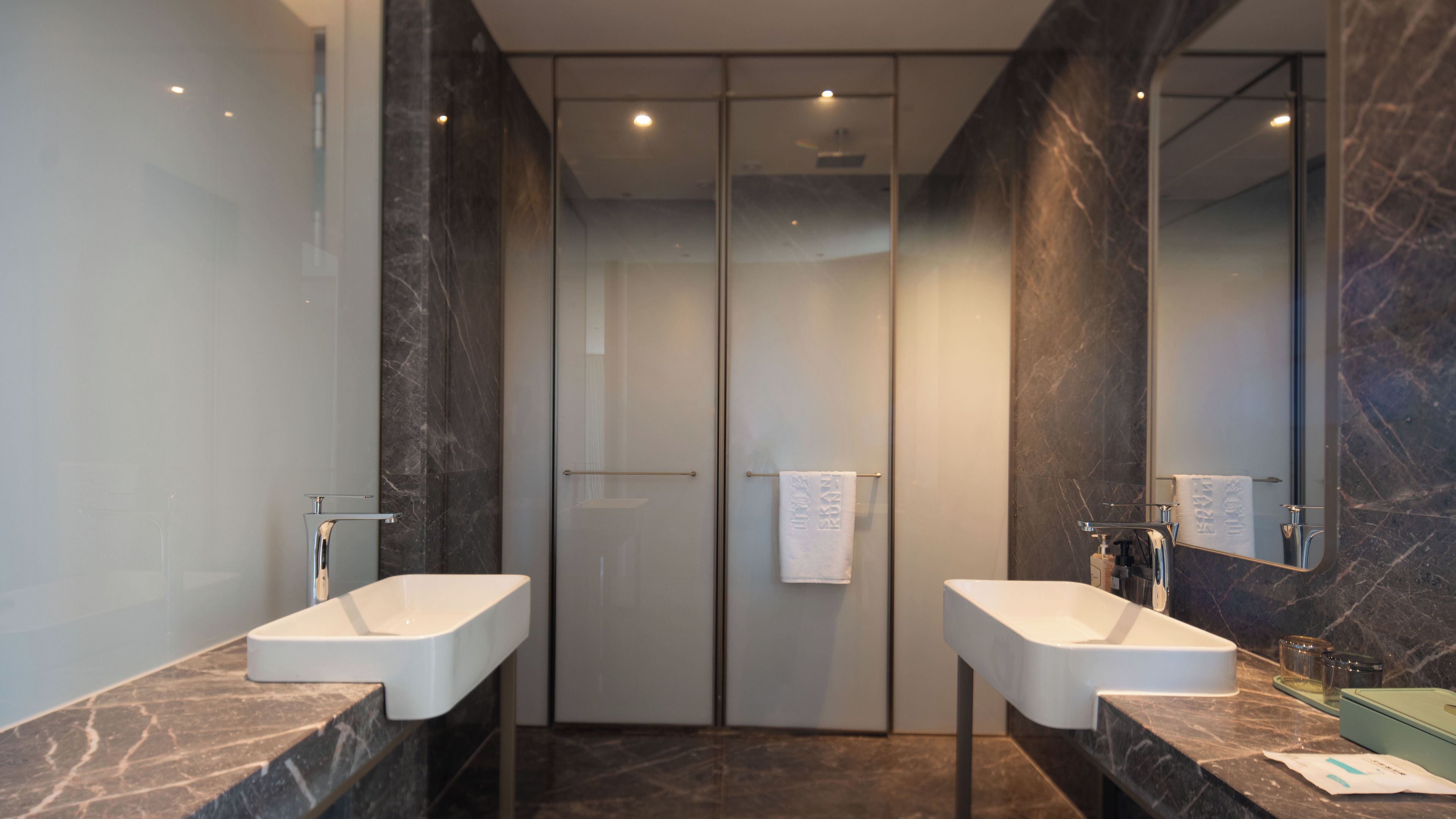 A modern bathroom with two sinks, a large mirror, and a glass door leading to a shower area.