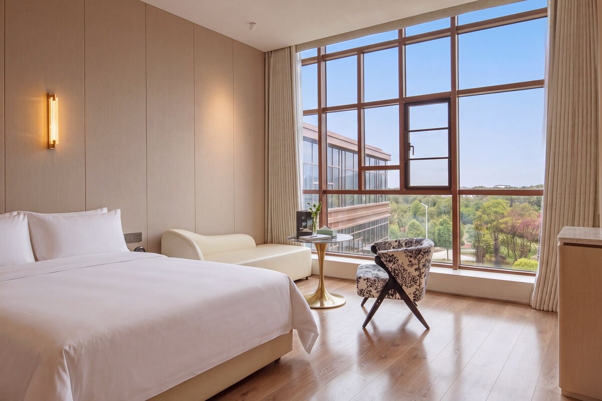 Ein Hotelzimmer mit einem großen Bett, einem Schlafsofa, einem Sessel, einem kleinen Tisch und Blick ins Freie.