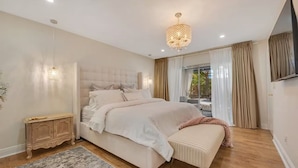 Un dormitorio con una cama grande, mesitas de noche, un candelabro y un televisor.