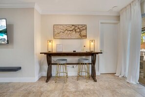 A dining area with a wooden table, two bar stools, a wall-mounted painting, and two wall sconces. - Casa Arkos 3BR Private Pool Beach & Everglades (Coral Springs)