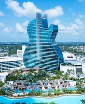 A modern building with a guitar-shaped design, surrounded by a resort area with multiple pools and overwater bungalows. - Casa Arkos 3BR Private Pool Beach & Everglades (Coral Springs)