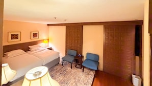 Una habitación de hotel con cama, dos sillas, una mesita, una lámpara y una puerta con diseño geométrico.