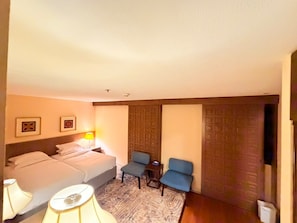 Ein Hotelzimmer mit einem Bett, zwei Stühlen, einem kleinen Tisch, einer Lampe und einer Tür mit einem geometrischen Muster.