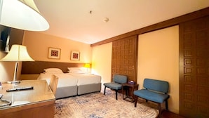 Una habitación de hotel con cama, escritorio con lámpara, silla y sofá azul.