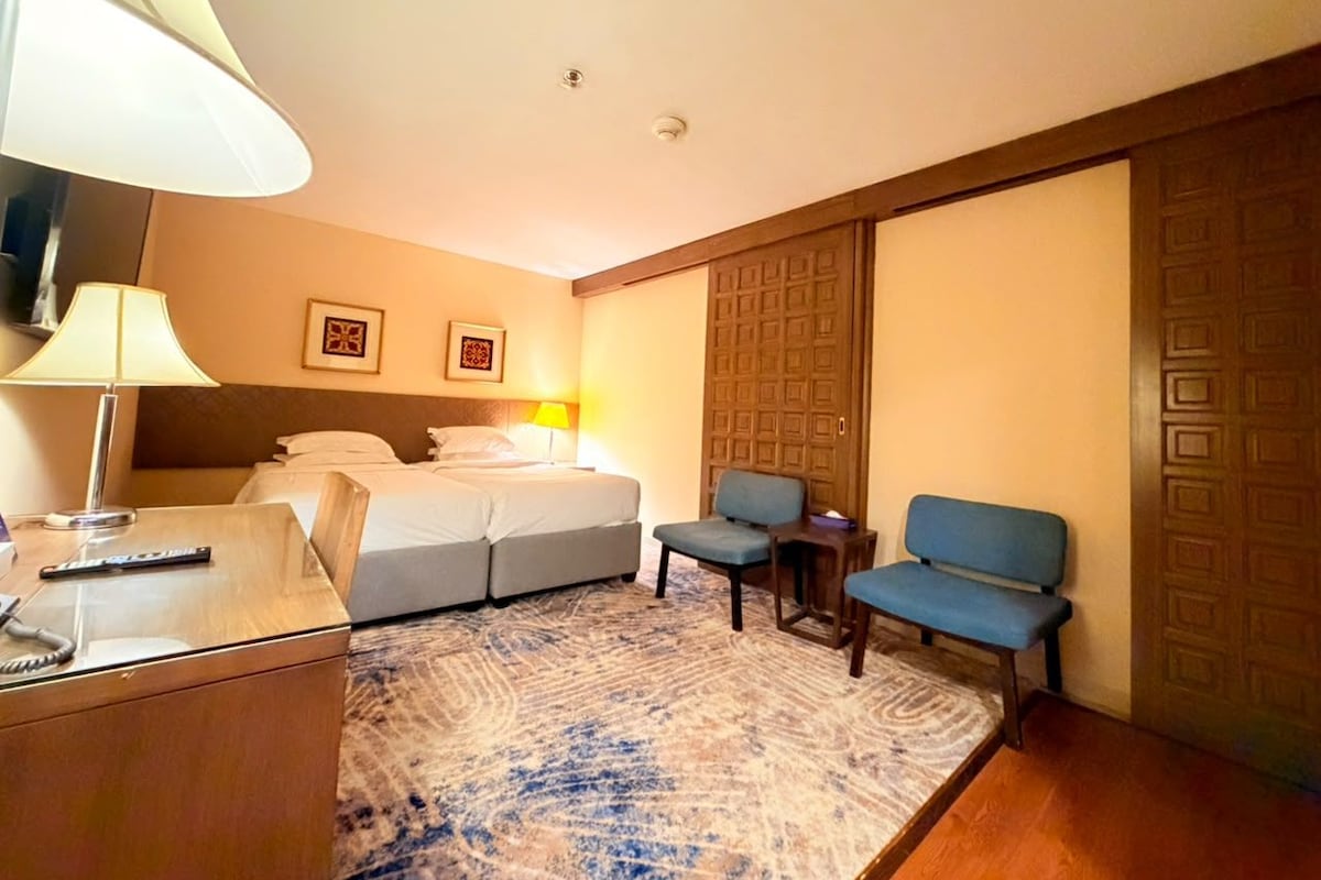 Ein Hotelzimmer mit Bett, Schreibtisch mit Lampe, Stuhl und blauem Sofa.