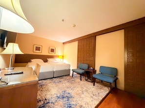 Ein Hotelzimmer mit Bett, Schreibtisch mit Lampe, Stuhl und blauem Sofa.
