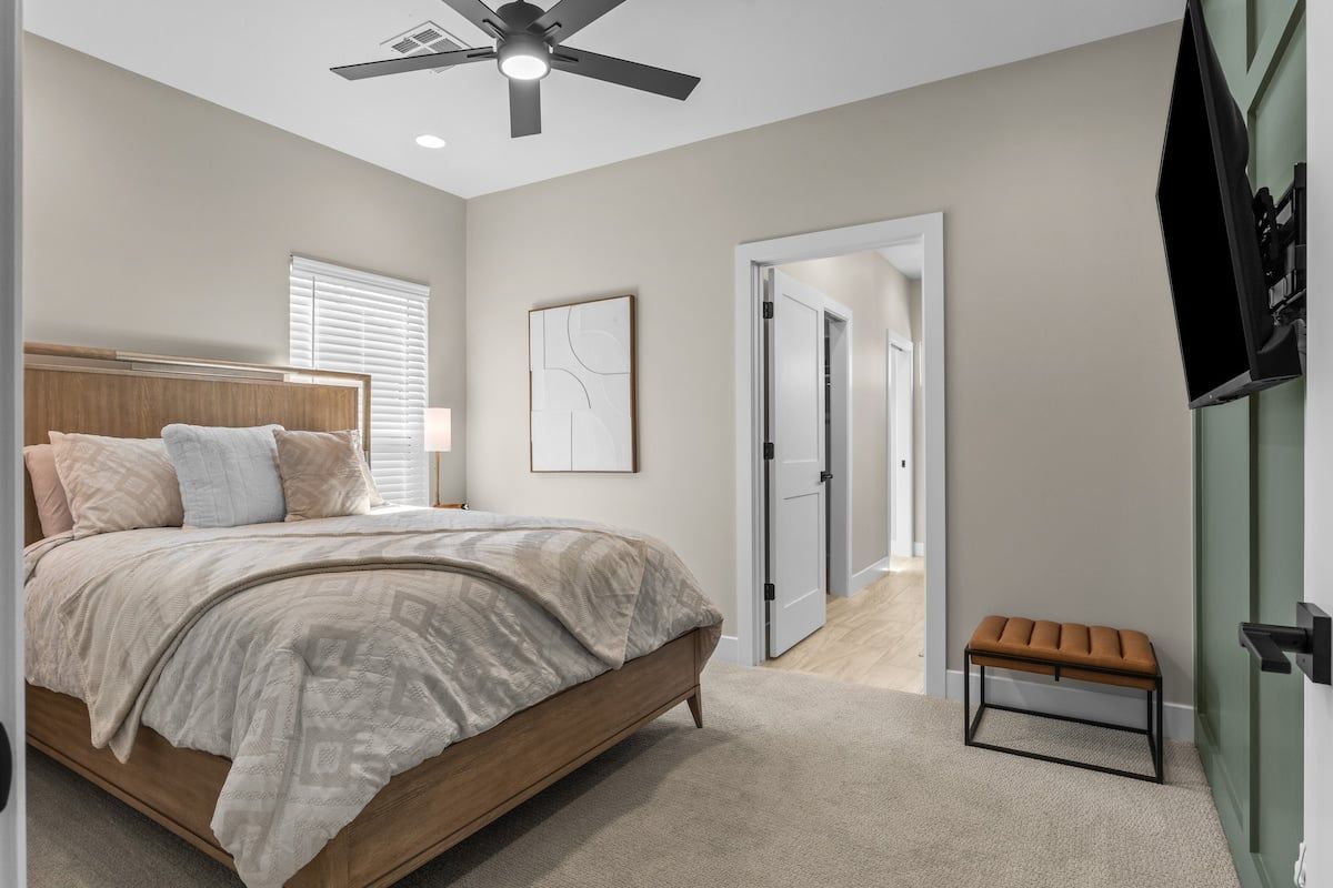 Un dormitorio con cama, ventilador de techo, una puerta que da a otra habitación y un banco.