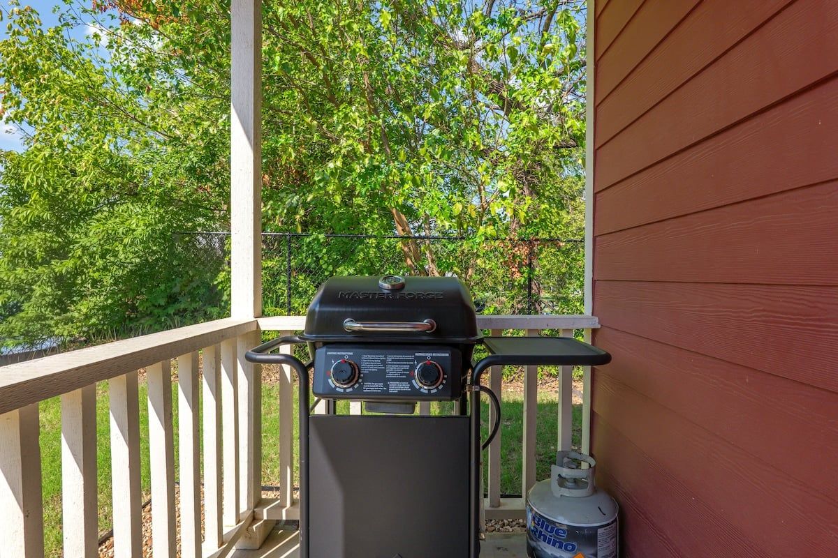 A barbecue grill on a porch with a view of trees and a house in the background.