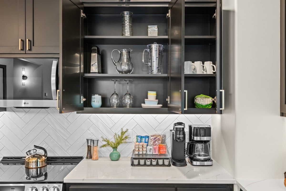 A modern kitchen with a built-in coffee station, a kettle, and a variety of glassware.