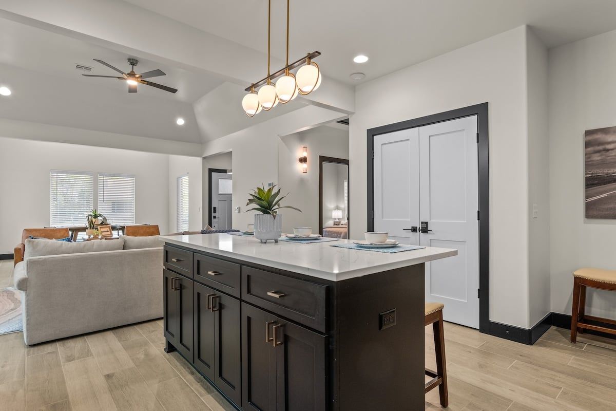 A modern kitchen with a central island, dark cabinetry, and a ceiling fan.