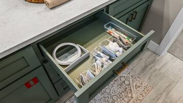A kitchen with a drawer containing kitchen utensils and a white cable.