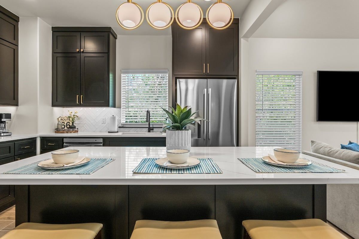A modern kitchen with dark cabinets, a stainless steel refrigerator, and a central island with seating.