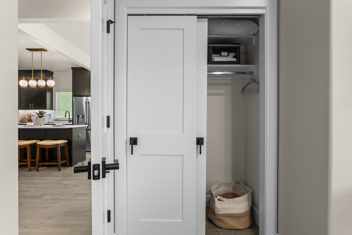 A white door with a black handle, leading to a closet with hanging space and a basket.