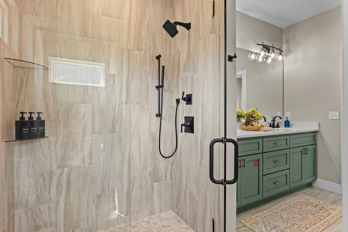 A modern bathroom with a glass-enclosed shower, a vanity with green cabinets, and a mirror above the sink.
