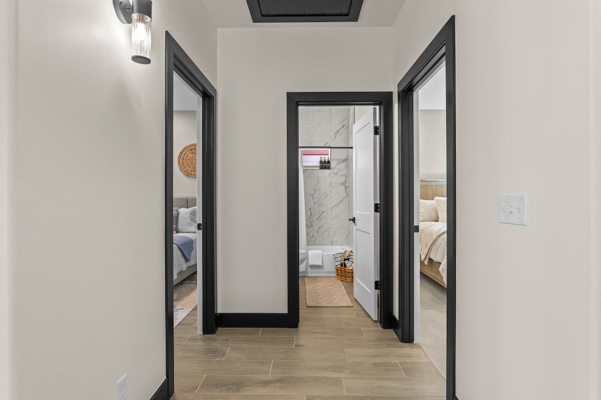 A hallway with a mirrored wall, leading to a bathroom with a marble wall and a bathtub.